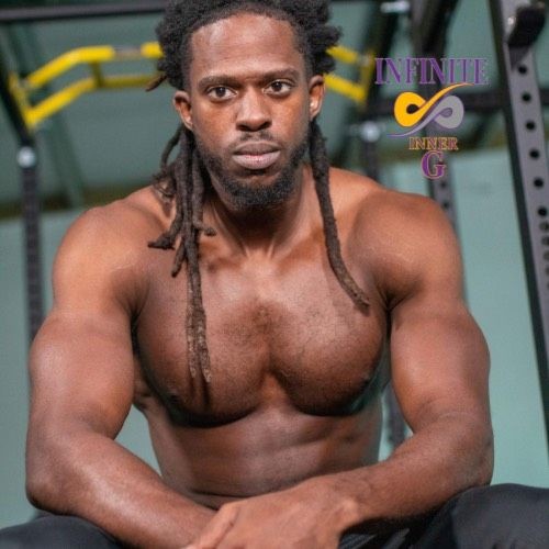 Muscular man with long hair and beard sitting in a gym, wearing a serious expression.